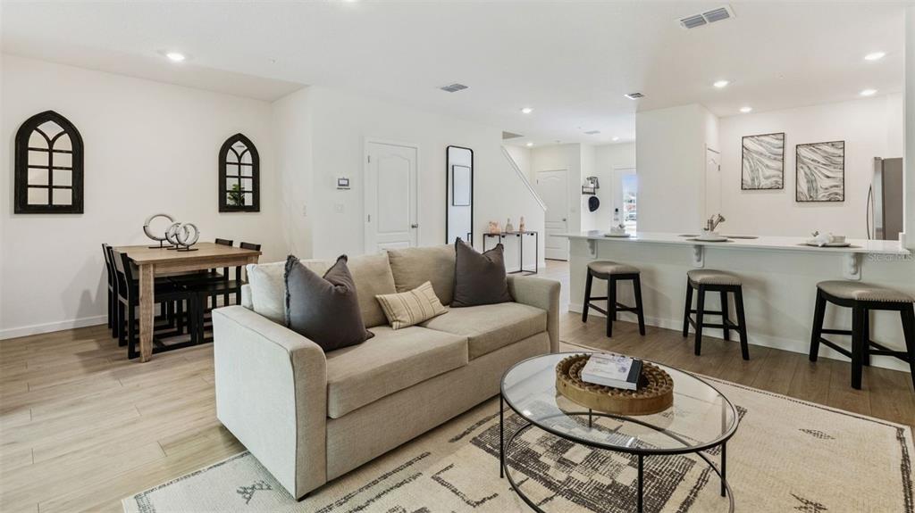 A bright open-concept living room features a beige sofa, dining area, and kitchen island — 3571 WYE OAK DRIVE, APOPKA, FL