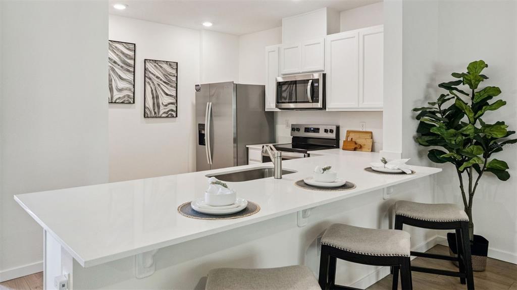A modern kitchen features a white quartz island, stainless steel appliances, and white cabinetry — 3571 WYE OAK DRIVE, APOPKA, FL