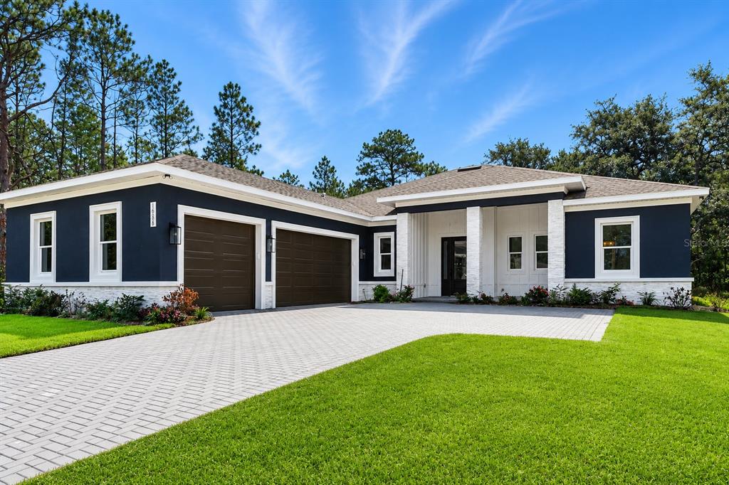 A modern single-story house with dark blue siding, white stone accents, and a paved driveway — 16098 MELLON ROAD, WEEKI WACHEE, FL