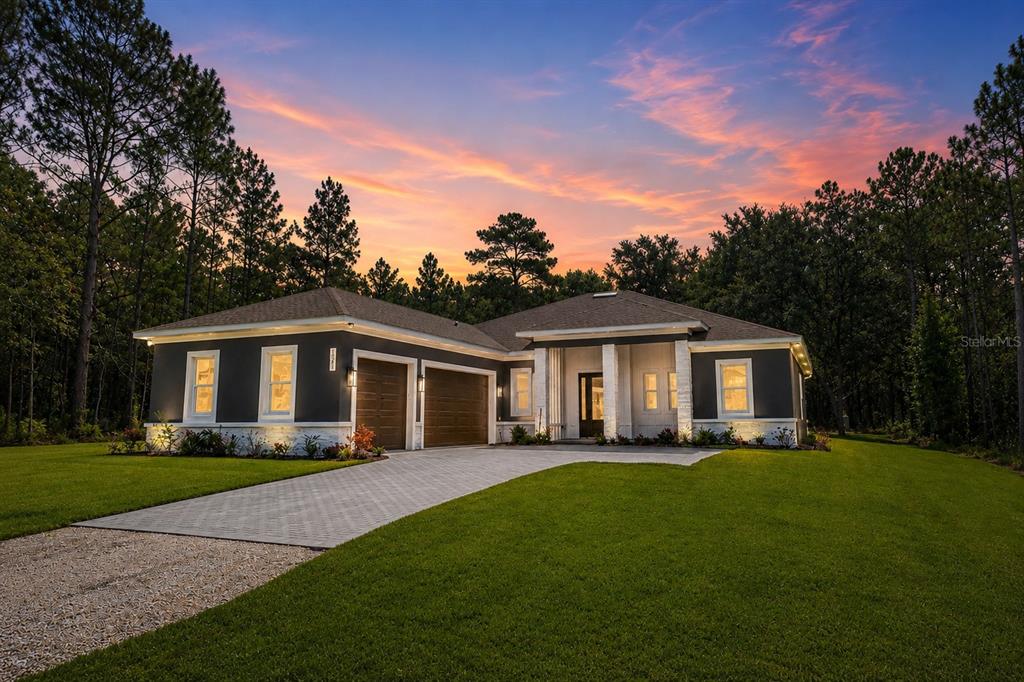 A modern single-story house with a dark gray exterior, stone accents, and a paved driveway — 16098 MELLON ROAD, WEEKI WACHEE, FL