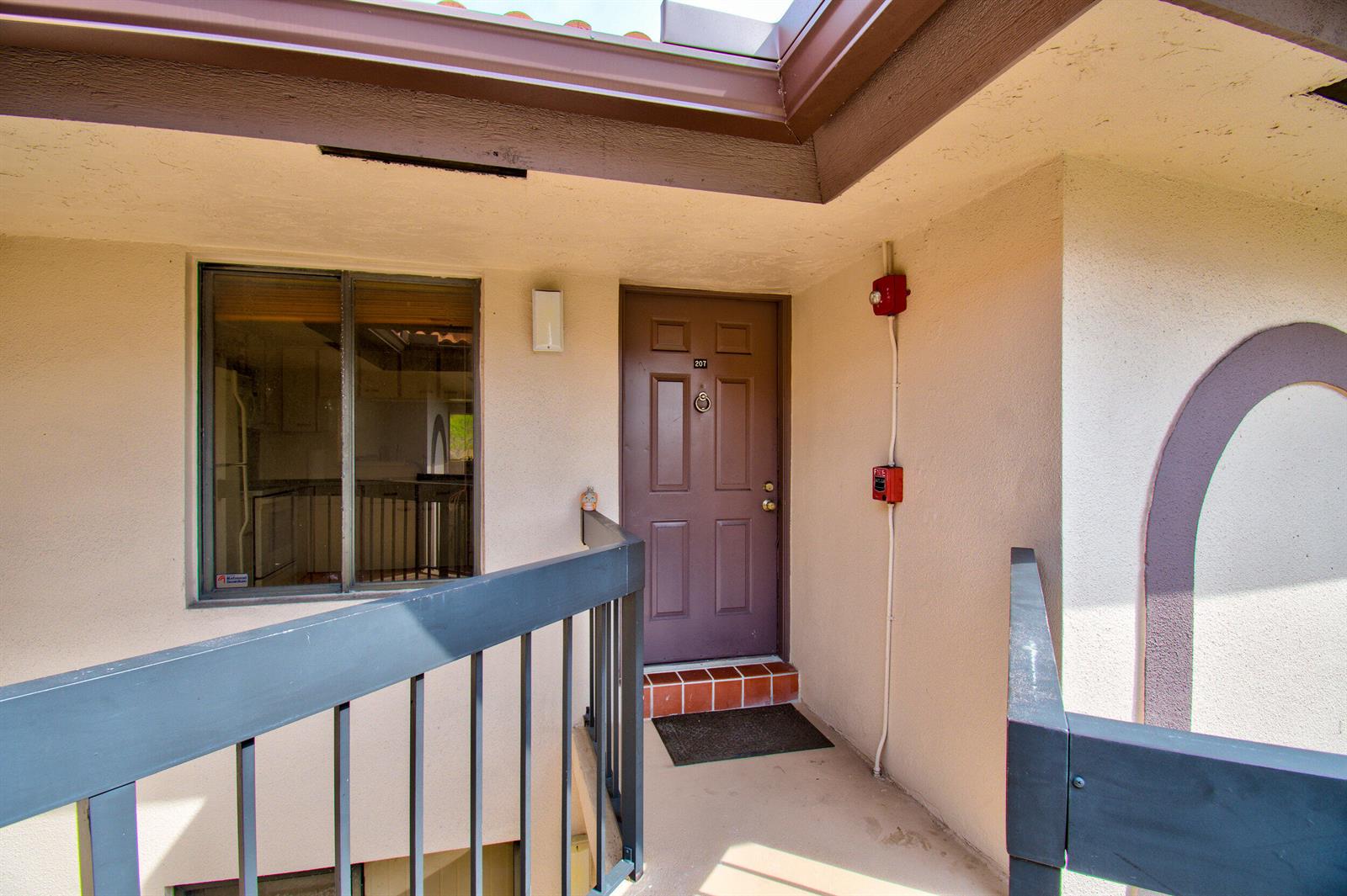 An exterior view of a brown apartment door labeled 207 with a balcony railing — 351 Club Circle # 207, Boca Raton FL 33487, BOCA RATON, FL