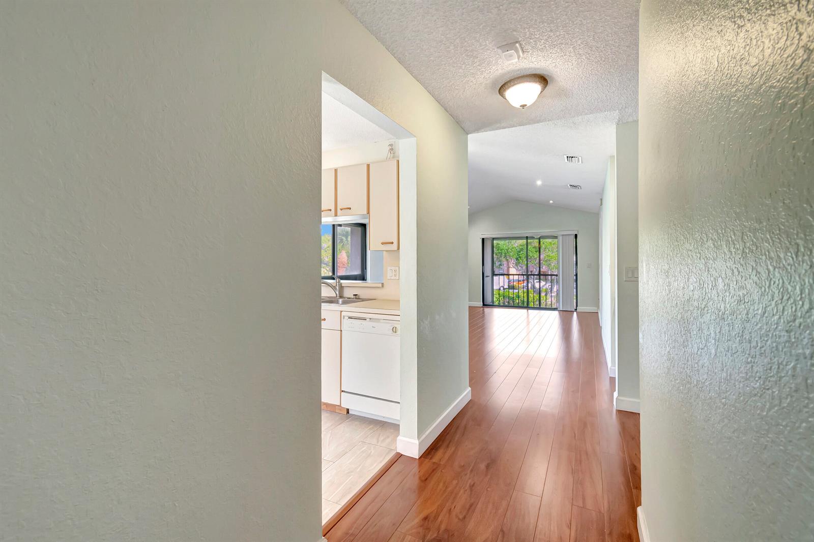 A hallway with wood flooring leads to a kitchen and a living area with sliding doors — 351 Club Circle # 207, Boca Raton FL 33487, BOCA RATON, FL