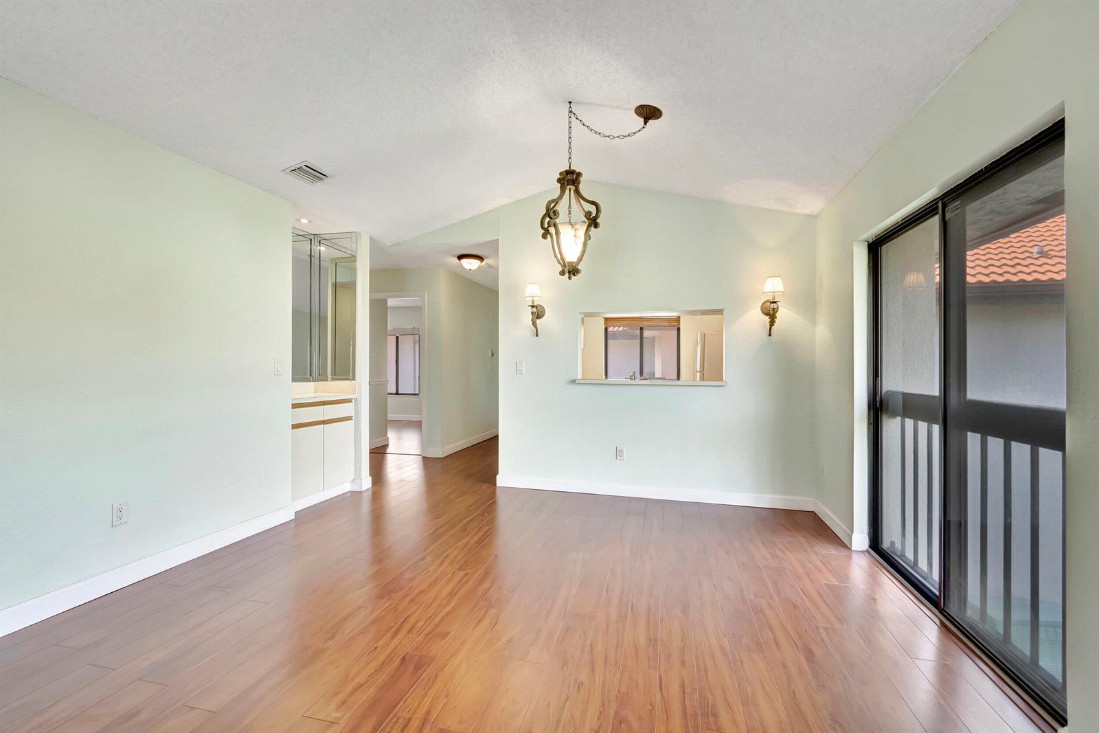 An empty dining room features light green walls, wood-look flooring, a chandelier, and sliding doors — 351 Club Circle # 207, Boca Raton FL 33487, BOCA RATON, FL