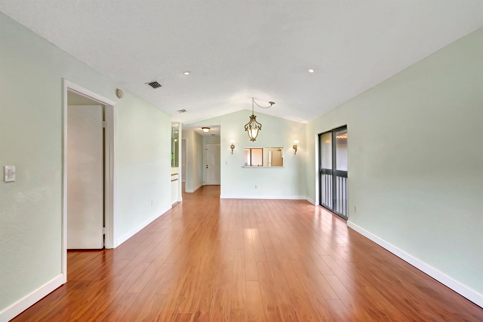 An empty room with light green walls, wood flooring, a vaulted ceiling, and a chandelier — 351 Club Circle # 207, Boca Raton FL 33487, BOCA RATON, FL