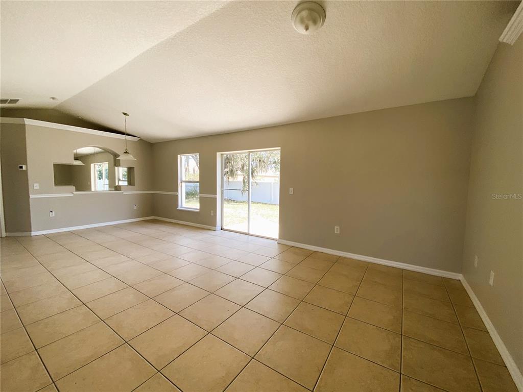 An empty living room features beige tile flooring, neutral walls, and a sliding glass door — 311 BACCARAT COURT, KISSIMMEE, FL