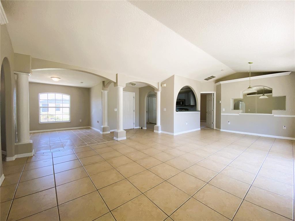 An open-concept living area features beige tile flooring, arched entryways, and decorative white columns — 311 BACCARAT COURT, KISSIMMEE, FL