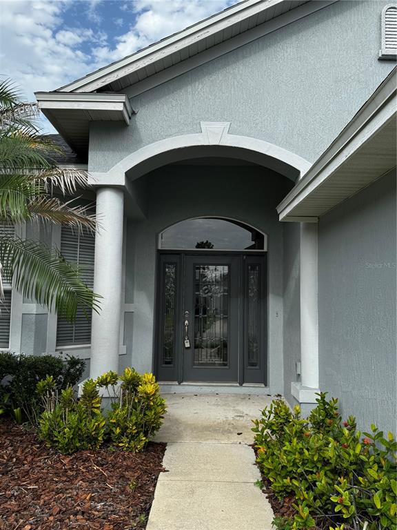 The exterior of a house features a gray stucco facade, arched entryway, and front door — 6871 EAGLE RIDGE LOOP, LAKELAND, FL