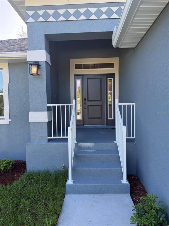 The exterior of a house features a blue stucco facade, white railings, and a front door — 4508 BRINTNALL STREET, PORT CHARLOTTE, FL