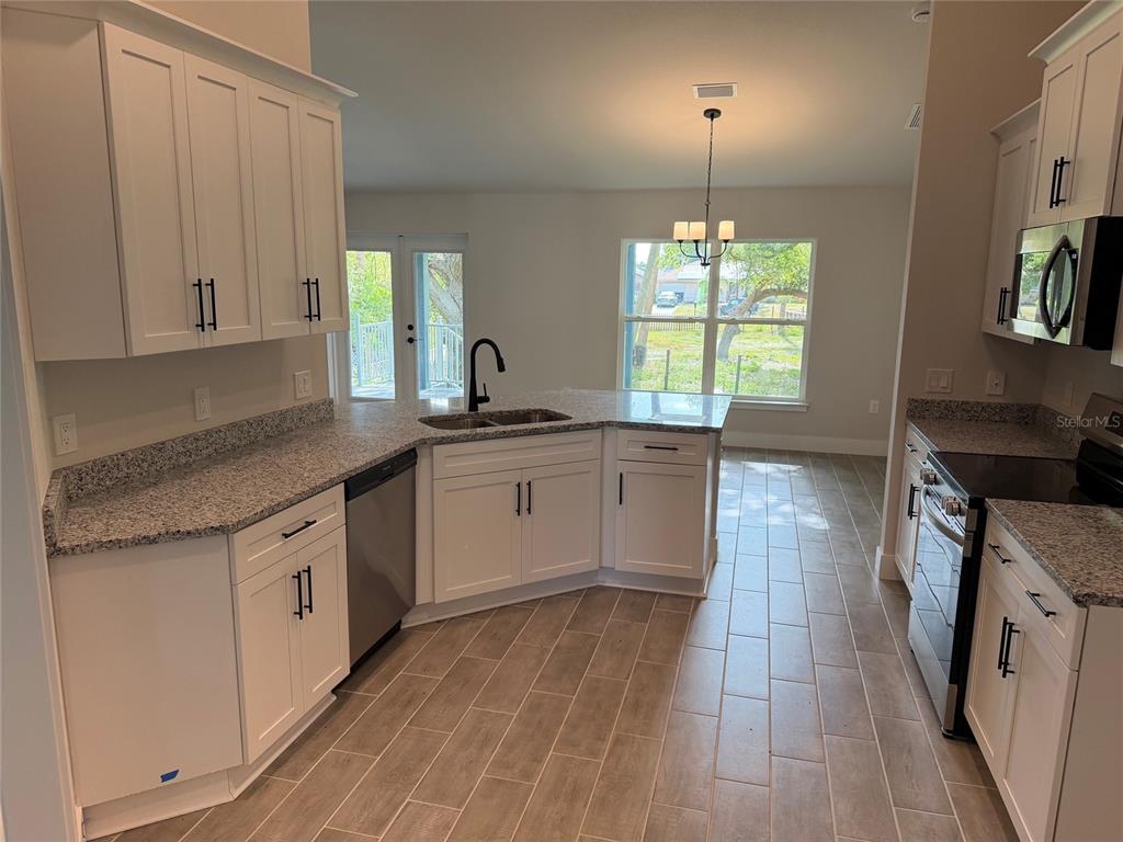A kitchen features white cabinets, granite countertops, stainless steel appliances, and light-colored tile flooring — 4508 BRINTNALL STREET, PORT CHARLOTTE, FL