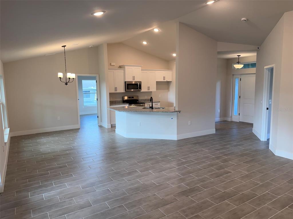 An open-concept kitchen with white cabinets and granite countertops overlooks a tiled living area — 4508 BRINTNALL STREET, PORT CHARLOTTE, FL