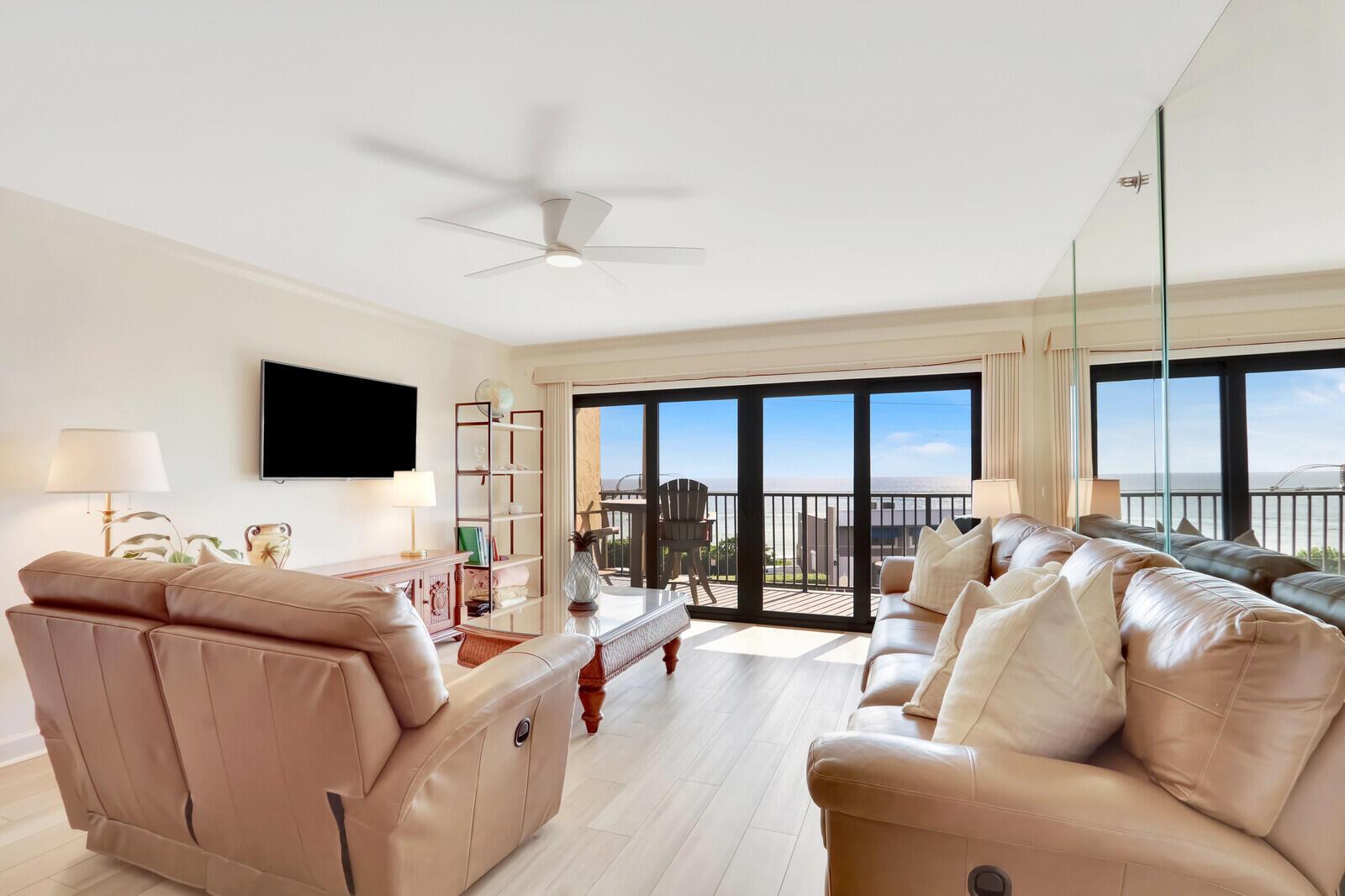 A living room with leather sofas, a ceiling fan, and sliding doors opening to a balcony — 1055 Ocean Drive # 403, Juno Beach FL 33408, JUNO BEACH, FL