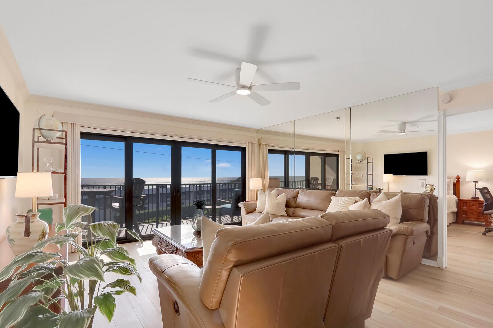 A living room with a leather sectional, ceiling fan, mirrored wall, and sliding glass balcony doors — 1055 Ocean Drive # 403, Juno Beach FL 33408, JUNO BEACH, FL