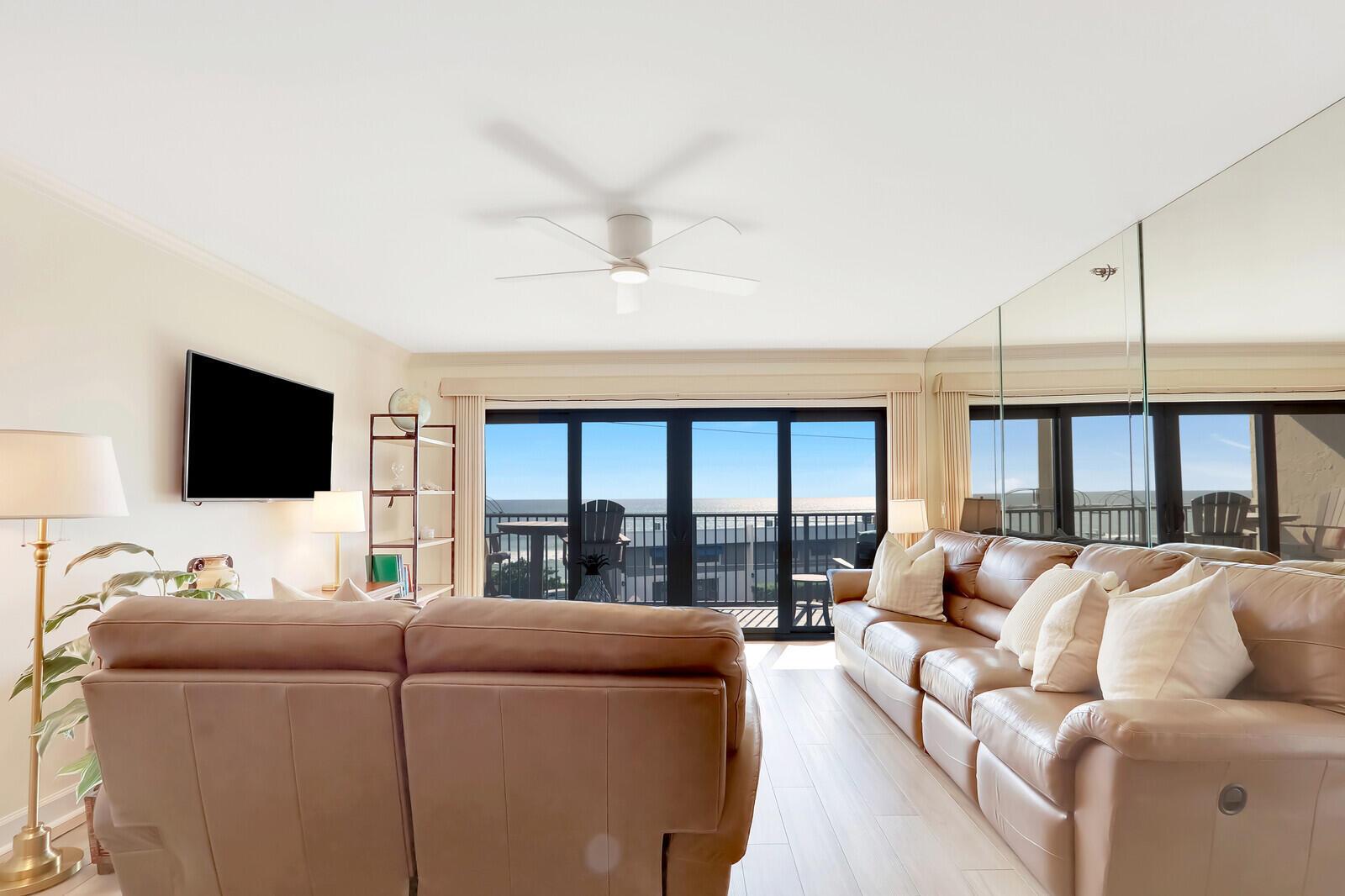 A living room features a leather sofa, a ceiling fan, and sliding doors to a balcony — 1055 Ocean Drive # 403, Juno Beach FL 33408, JUNO BEACH, FL