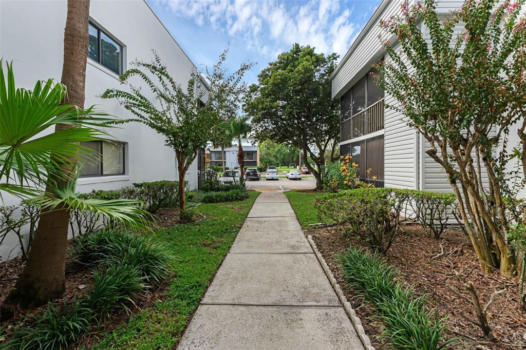 A concrete walkway leads between two residential buildings toward a parking lot with several cars — 2597 OAK PARK WAY UNIT 205, ORLANDO, FL