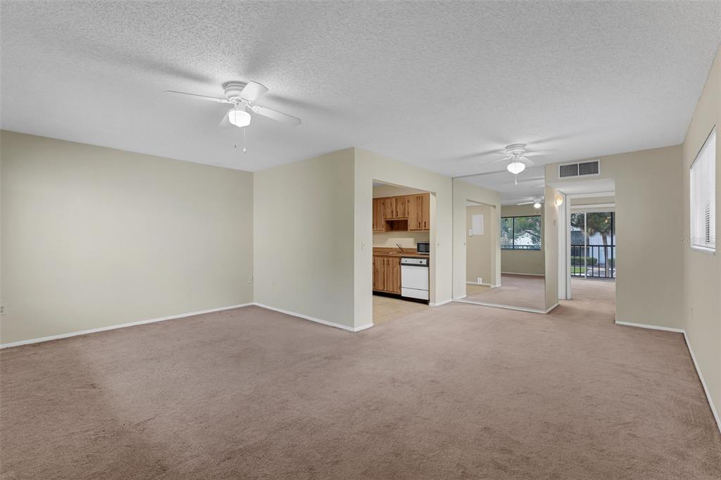 A carpeted living room with two ceiling fans leads to a kitchen and sliding glass doors — 2597 OAK PARK WAY UNIT 205, ORLANDO, FL