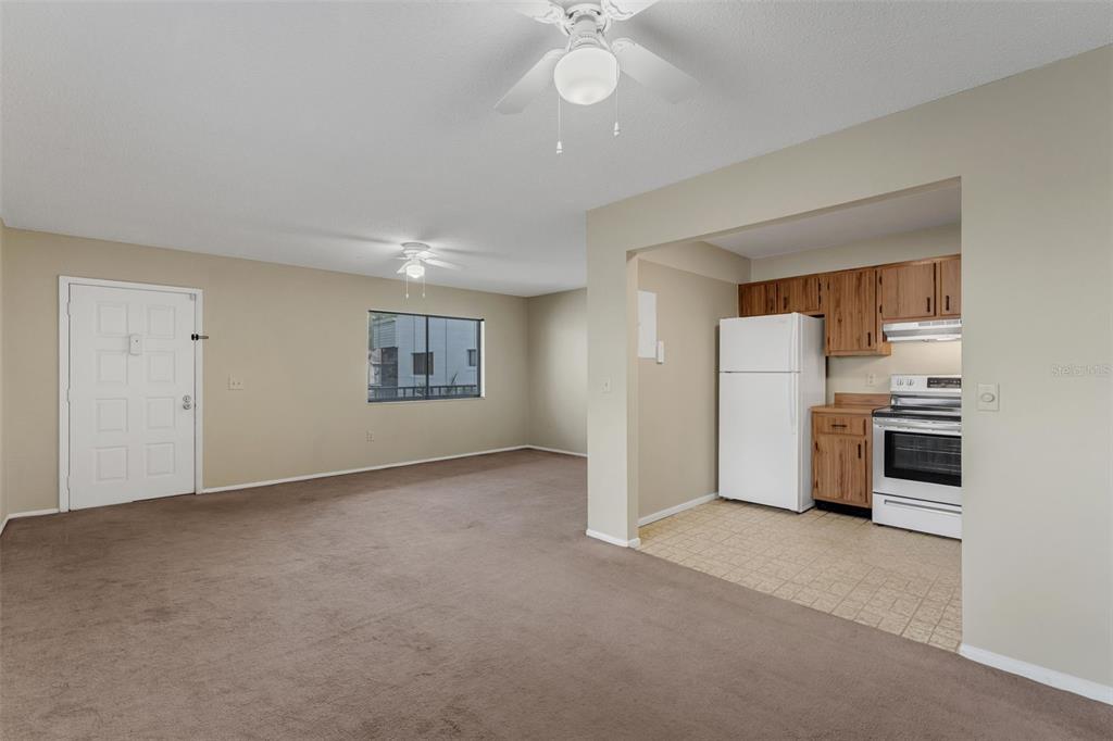 A carpeted living room opens into a kitchen with white appliances and wood cabinets — 2597 OAK PARK WAY UNIT 205, ORLANDO, FL