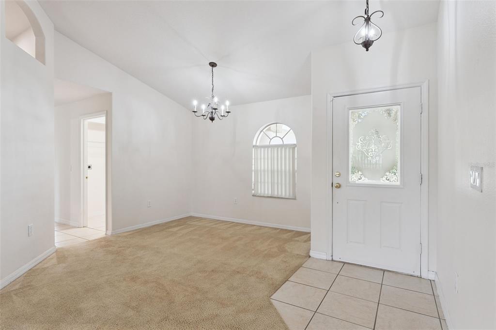 An entryway with tiled flooring leads to a carpeted room featuring a chandelier and window — 3042 WILD PEPPER AVENUE, DELTONA, FL
