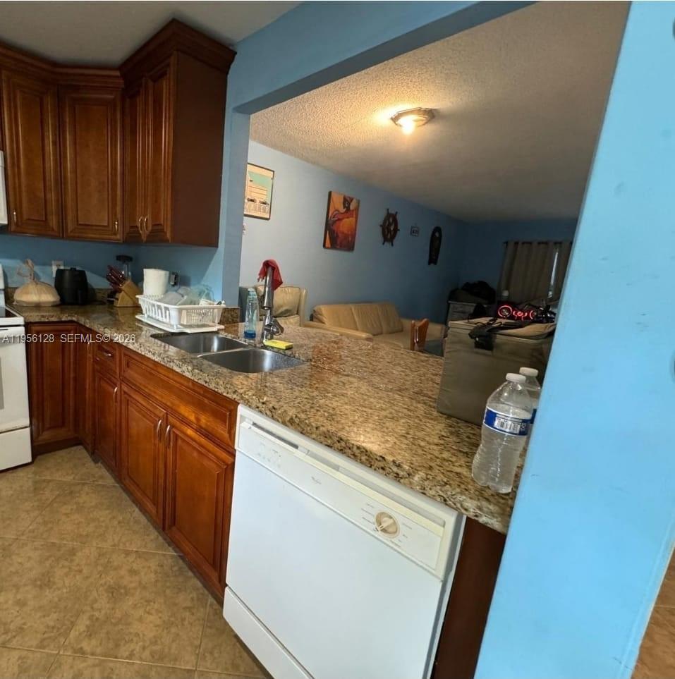 A kitchen with wood cabinets and granite countertops overlooks a living area with blue walls — 4321 NW 9th Ave # 104, Deerfield Beach FL 33064, DEERFIELD BEACH, FL