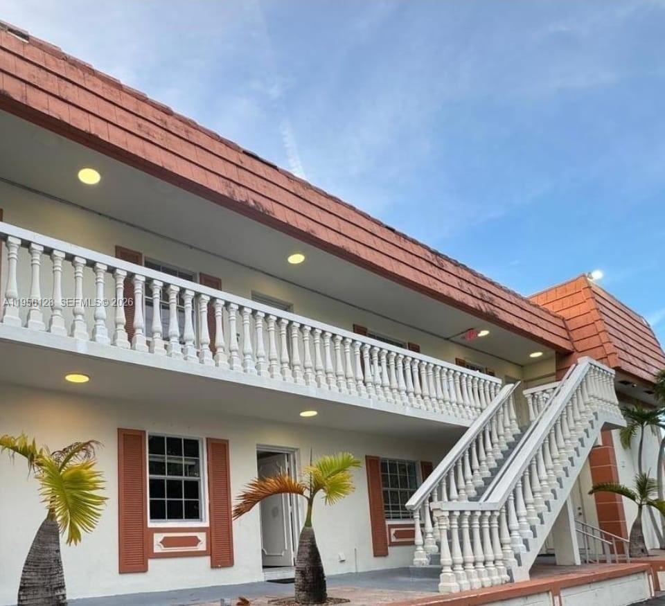 A two-story building exterior features white walls, brown shutters, and a white balustrade staircase — 4321 NW 9th Ave # 104, Deerfield Beach FL 33064, DEERFIELD BEACH, FL