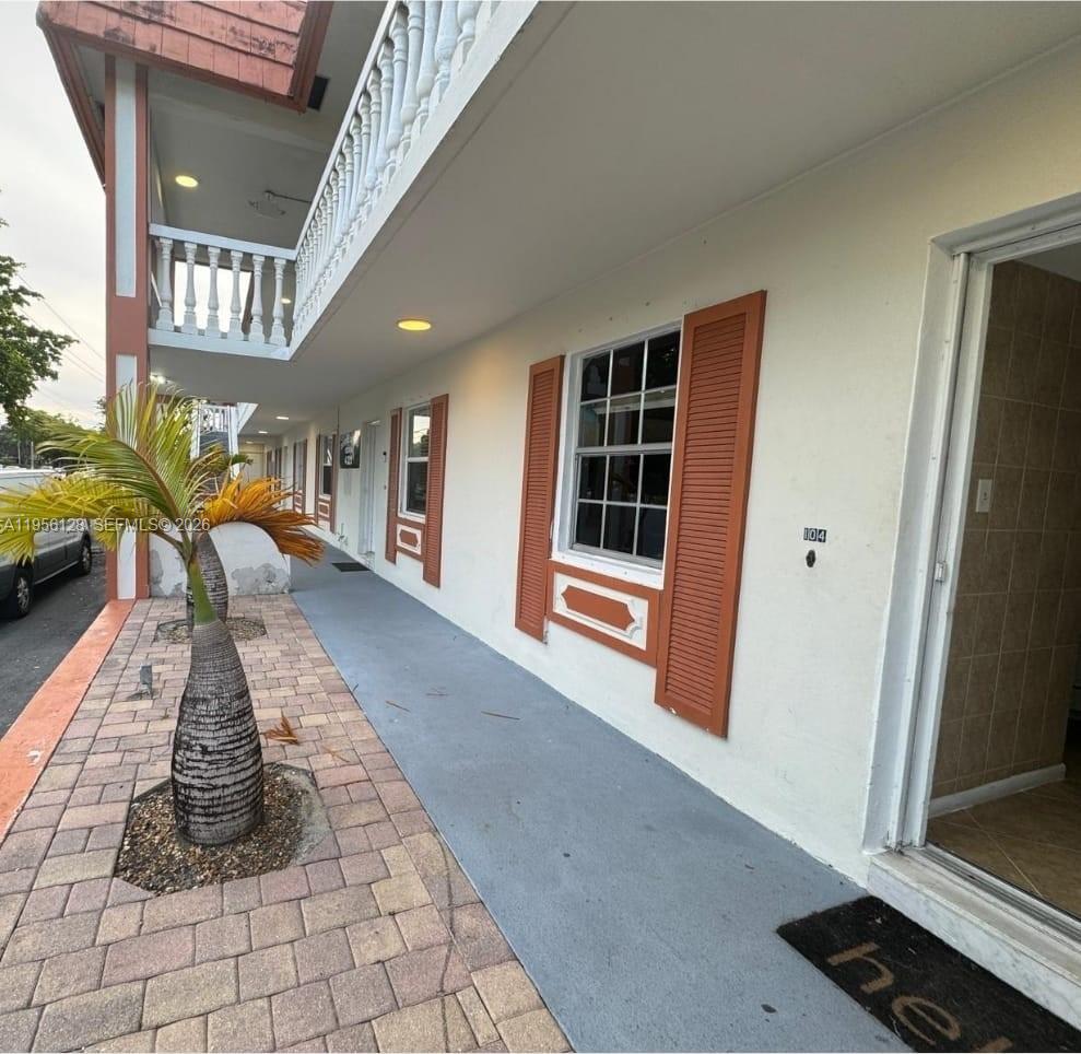 A ground-level apartment entrance with a paved walkway, palm tree, and orange-trimmed windows — 4321 NW 9th Ave # 104, Deerfield Beach FL 33064, DEERFIELD BEACH, FL
