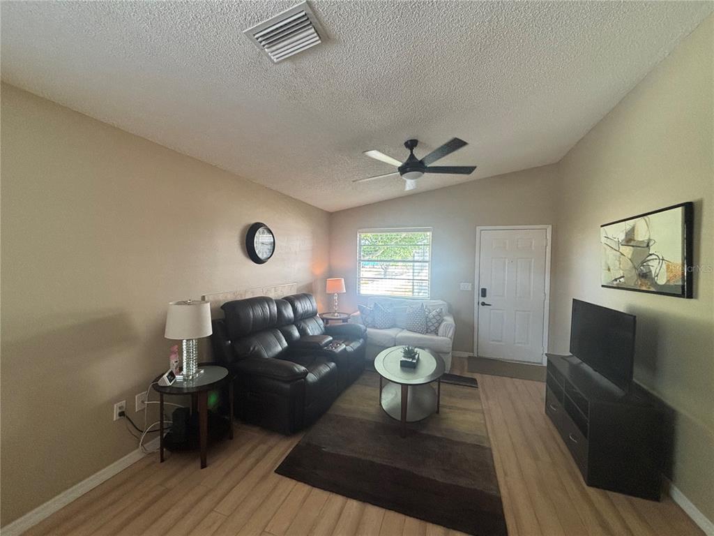 A living room features light wood flooring, a black leather sofa, and a television console — 3866 59TH AVENUE W UNIT 3866, BRADENTON, FL