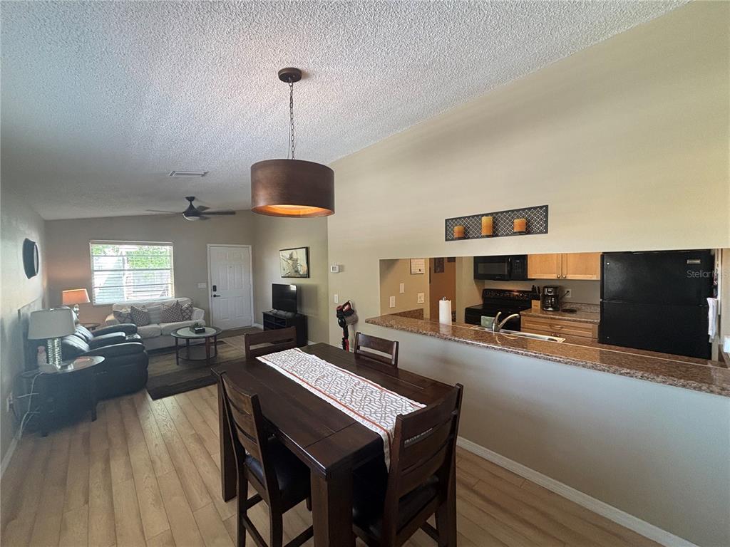 An open-concept living and dining area features wood-look flooring, a kitchen pass-through, and pendant lighting — 3866 59TH AVENUE W UNIT 3866, BRADENTON, FL