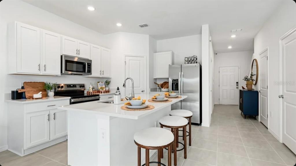 A modern kitchen features white cabinetry, stainless steel appliances, and a central island with seating — 10798 ECLIPSE STREET, SARASOTA, FL