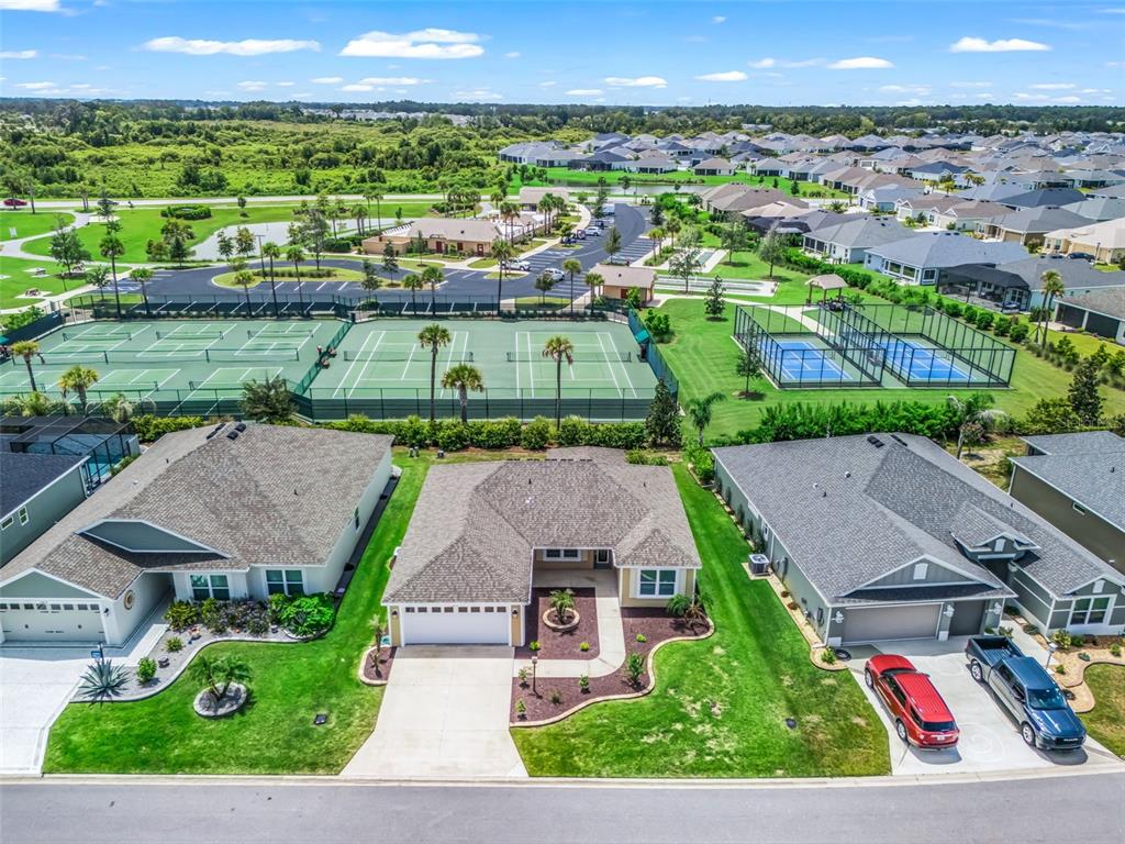 An aerial view shows three suburban houses situated directly across from tennis and pickleball courts — 2816 NAVY HILL CIRCLE, THE VILLAGES, FL