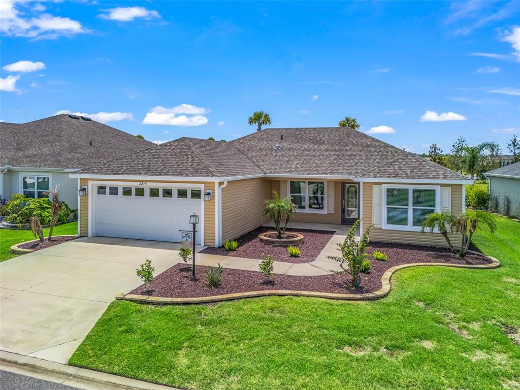 A tan single-story house with a two-car garage, shingled roof, and landscaped front yard — 2816 NAVY HILL CIRCLE, THE VILLAGES, FL