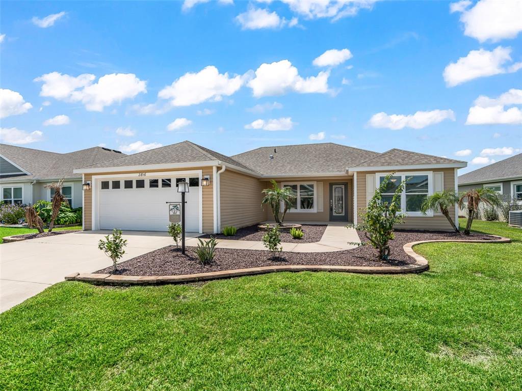 A single-story house with tan siding, a two-car garage, and a landscaped front yard — 2816 NAVY HILL CIRCLE, THE VILLAGES, FL