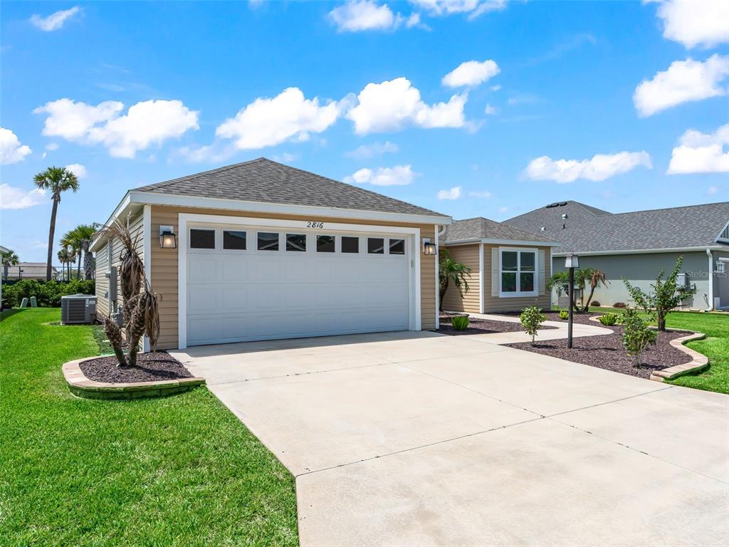 A tan house with a two-car garage, concrete driveway, and landscaped front yard under blue skies — 2816 NAVY HILL CIRCLE, THE VILLAGES, FL