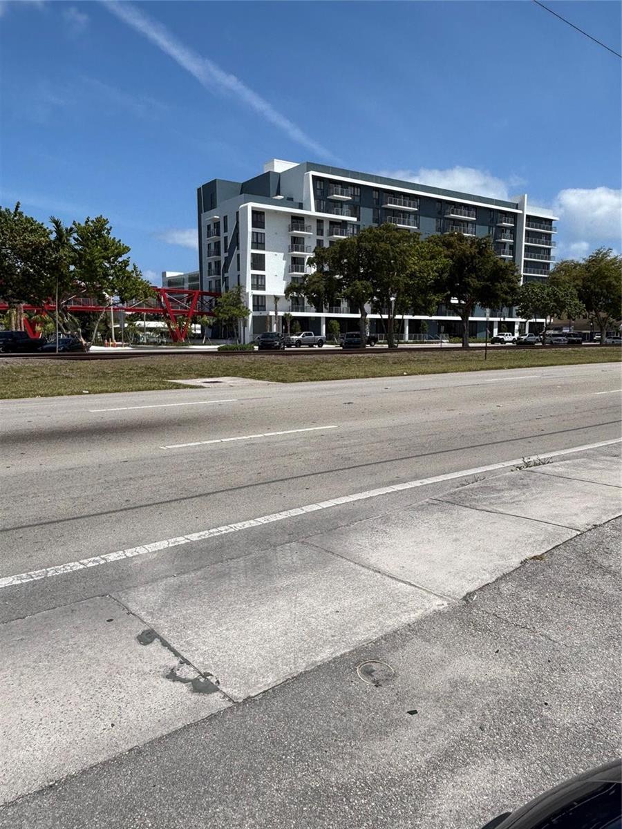 A modern multi-story apartment building stands behind a road and a red pedestrian bridge — 2117 Polk Street, Hollywood FL 33020, HOLLYWOOD, FL