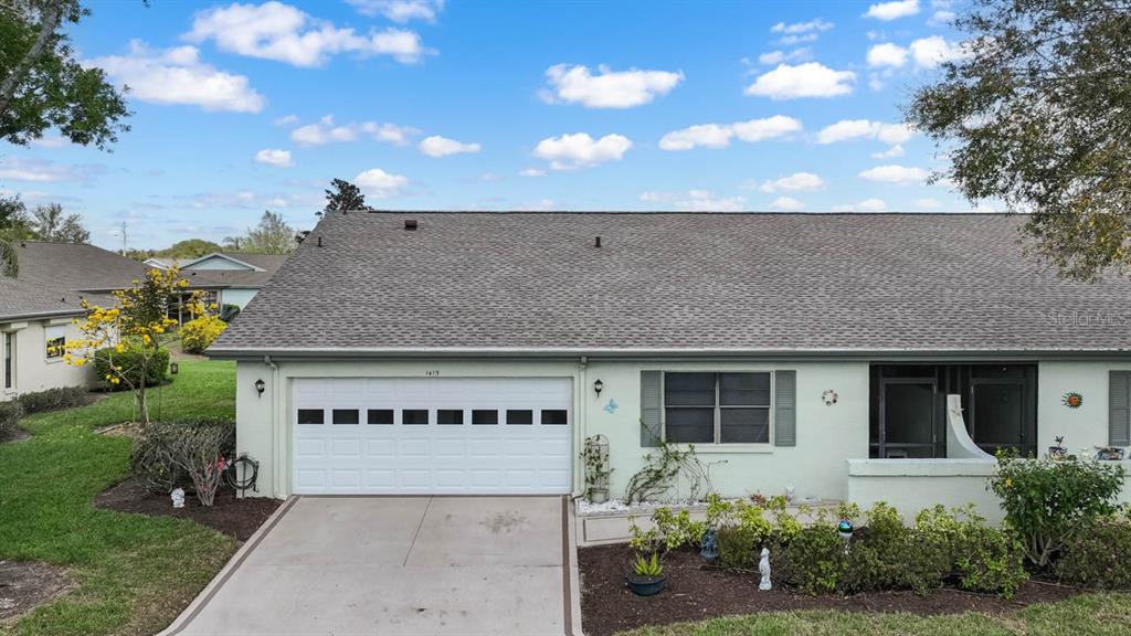 A light green single-story house features a white garage door and a screened-in front entryway — 1415 LANGLEY DRIVE, SUN CITY CENTER, FL