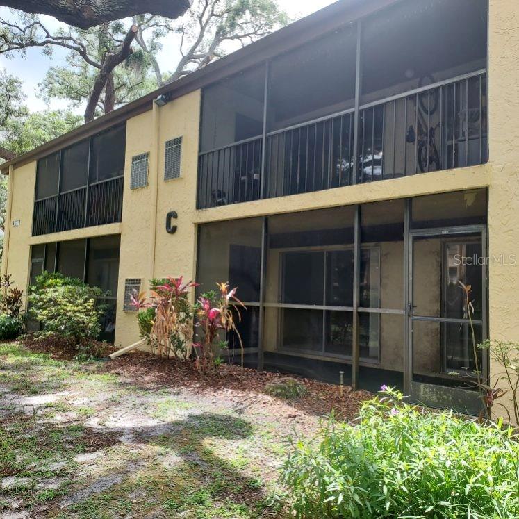 A two-story yellow apartment building features screened-in balconies and patios on both levels — 14111 MOSSY GLEN LANE UNIT 101C, TAMPA, FL