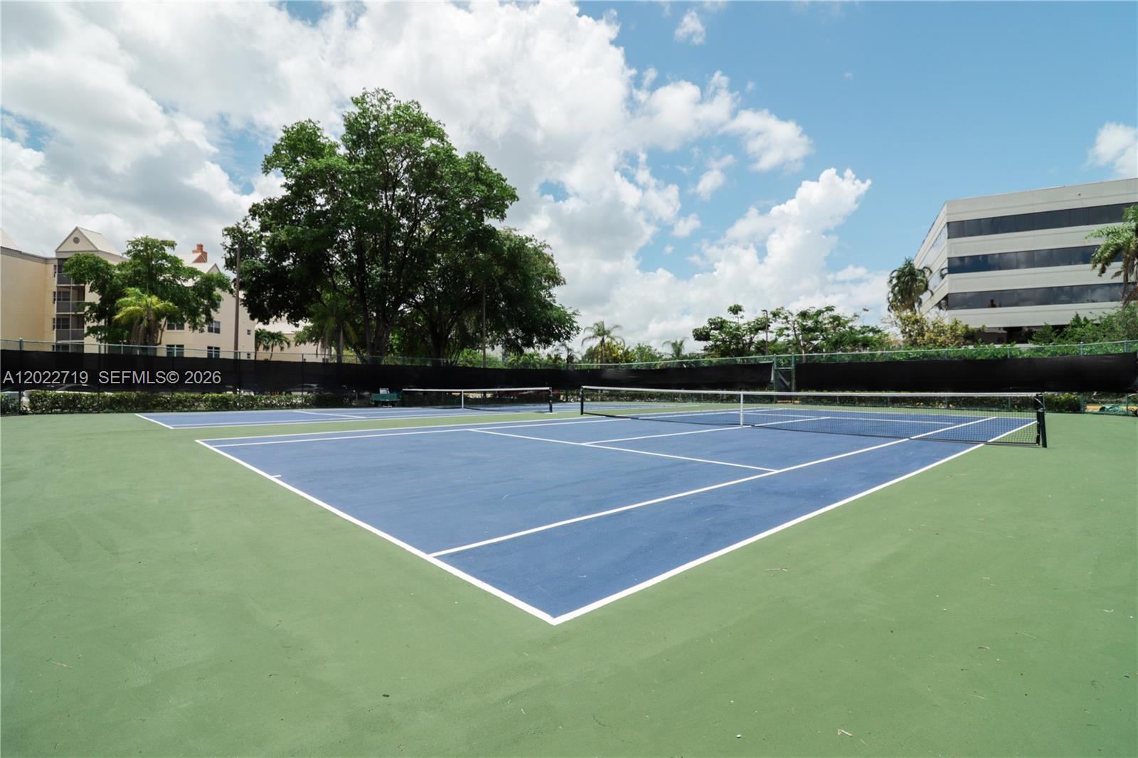 A blue and green outdoor tennis court is surrounded by a black fence and trees — 8245 Lake Dr # 405, Doral FL 33166, DORAL, FL