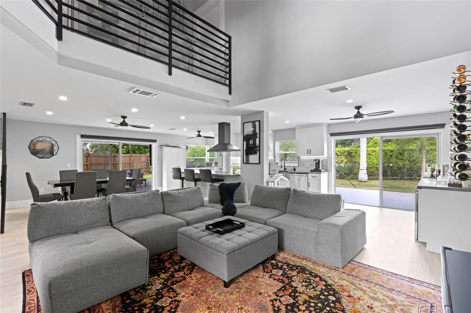 A spacious open-concept living room with a gray sectional, lofted balcony, and sliding glass doors — 133 SW 159th Way, Sunrise FL 33326, SUNRISE, FL