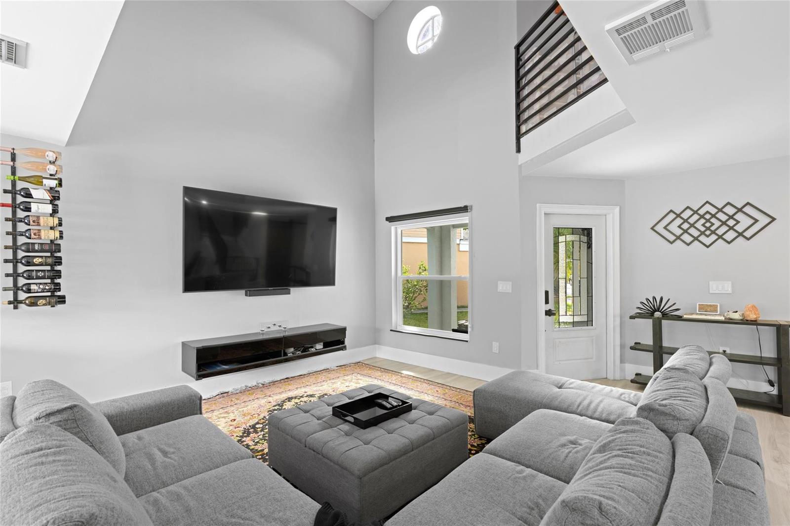 A living room features a vaulted ceiling, gray sectional sofa, wall-mounted television, and wine rack — 133 SW 159th Way, Sunrise FL 33326, SUNRISE, FL