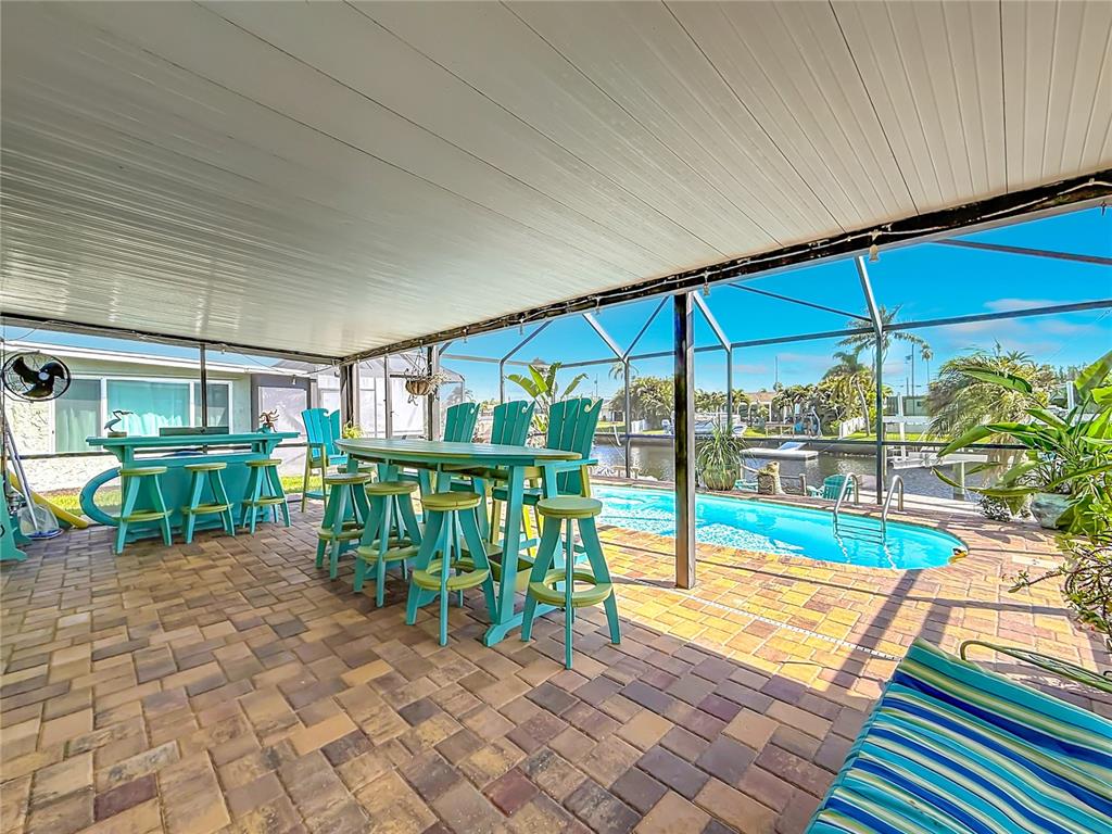 A covered patio features a dining set and bar stools overlooking a swimming pool and canal — 4046 FLORAMAR TERRACE, NEW PORT RICHEY, FL