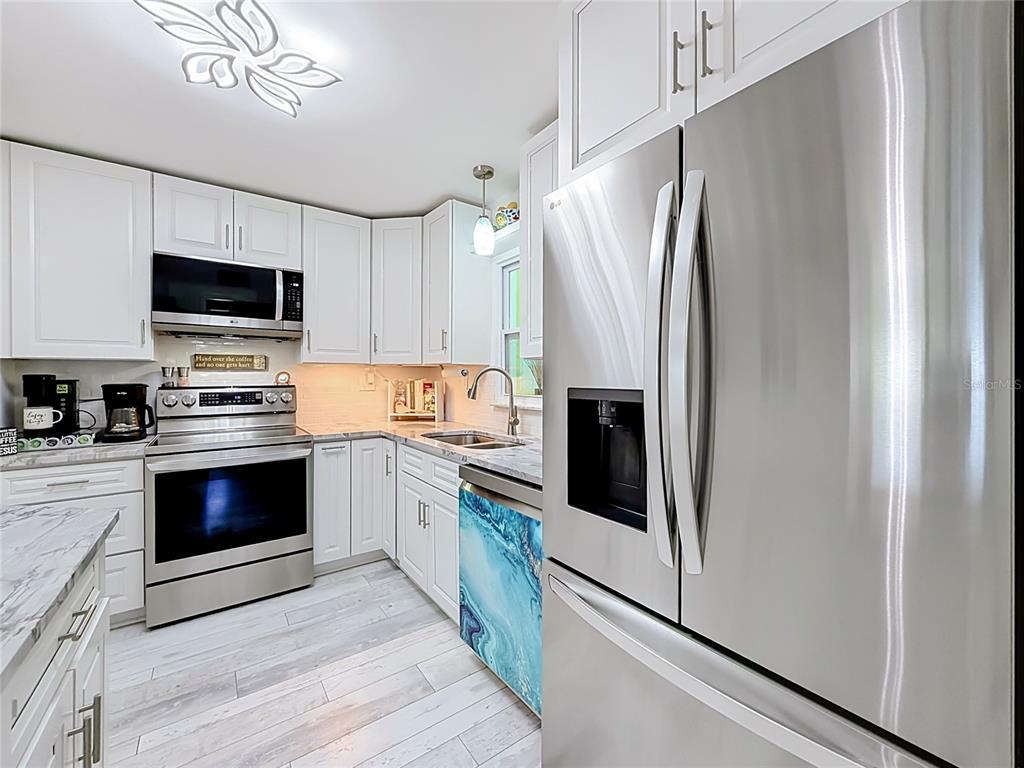 A kitchen with white cabinets, stainless steel appliances, marble-look countertops, and a blue patterned dishwasher — 4046 FLORAMAR TERRACE, NEW PORT RICHEY, FL