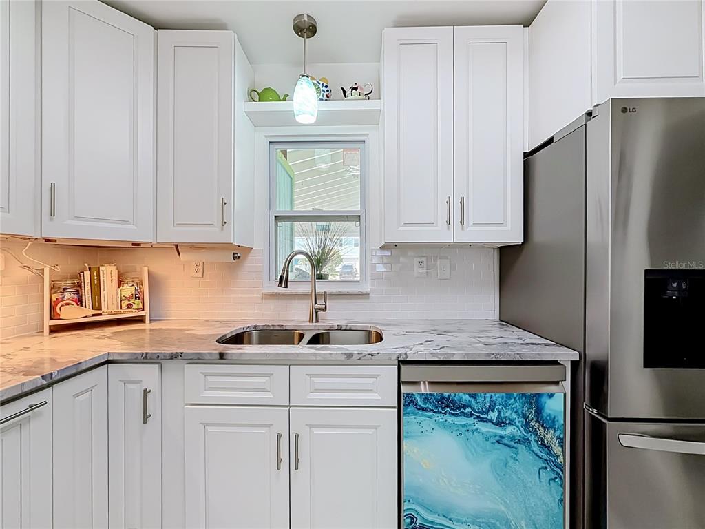 A kitchen features white cabinets, marble-look countertops, a stainless steel dishwasher, and a blue-patterned appliance — 4046 FLORAMAR TERRACE, NEW PORT RICHEY, FL