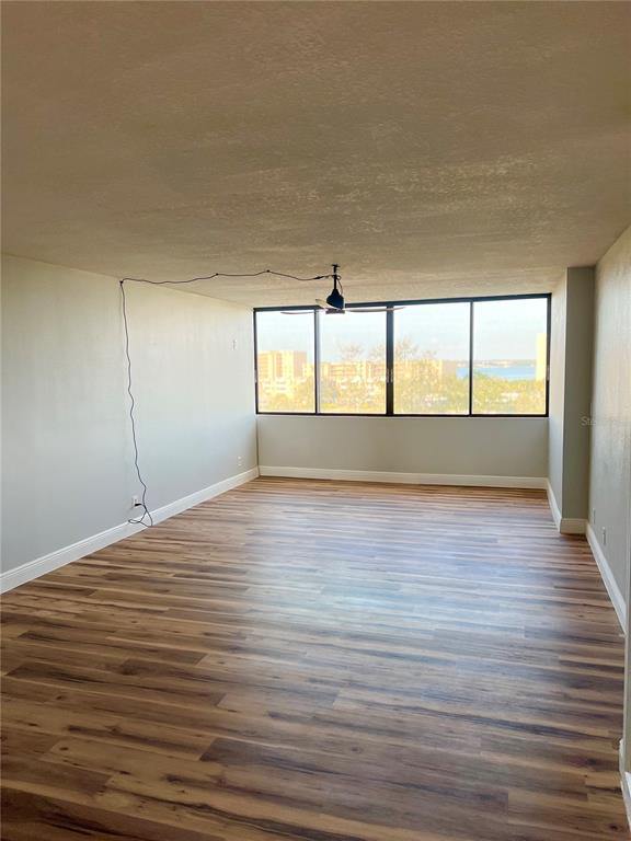 An empty room features light wood-look flooring, a ceiling fan, and large windows with water views — 2621 COVE CAY DRIVE UNIT 703, CLEARWATER, FL