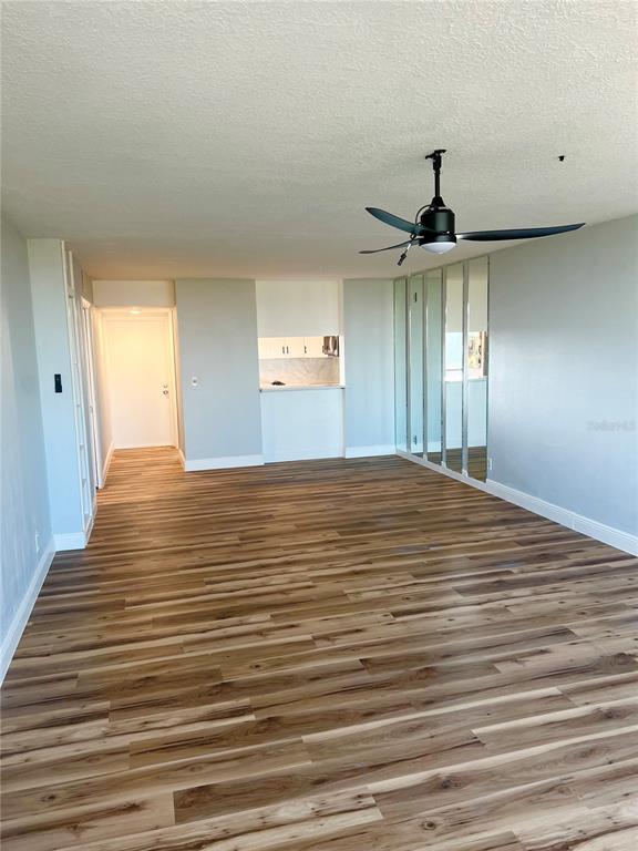 An empty room features wood-look flooring, a ceiling fan, and a mirrored wall — 2621 COVE CAY DRIVE UNIT 703, CLEARWATER, FL