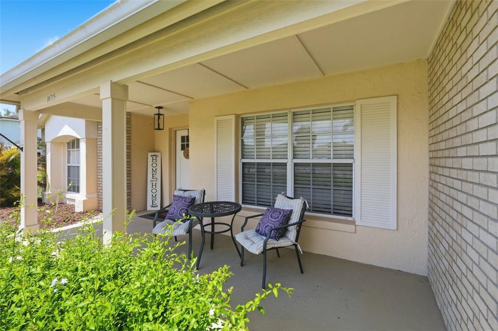 A covered front porch features a small table, two chairs, and a brick exterior wall — 14715 GREATER PINES BOULEVARD, CLERMONT, FL