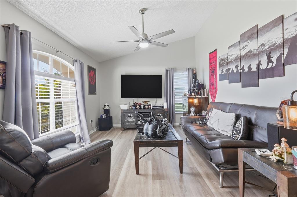 A living room features a leather sofa, a recliner, a television, and a ceiling fan — 14715 GREATER PINES BOULEVARD, CLERMONT, FL