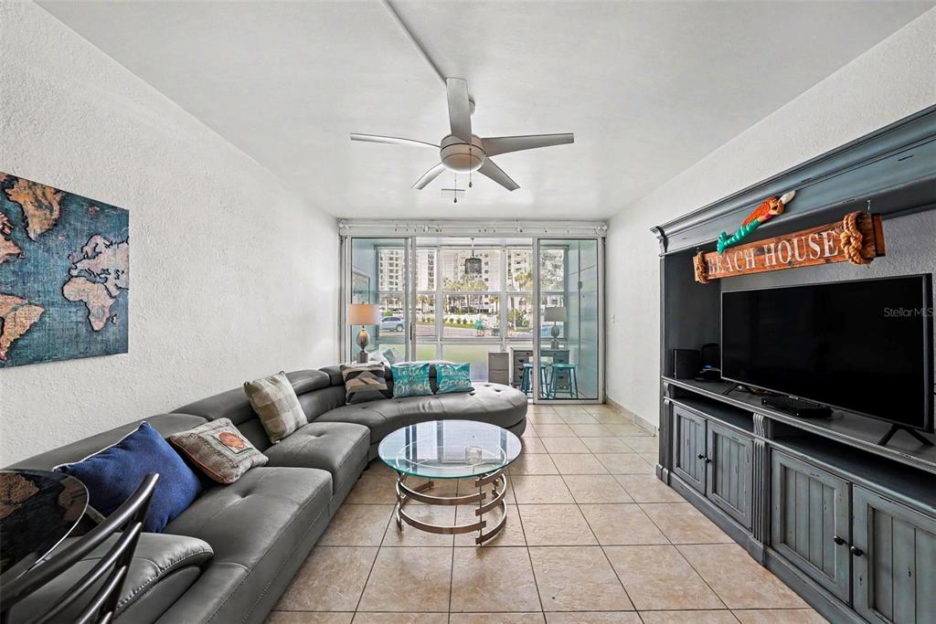 A living room features a gray sectional sofa, a glass coffee table, and a media console — 7050 SUNSET WAY UNIT 11, ST PETE BEACH, FL