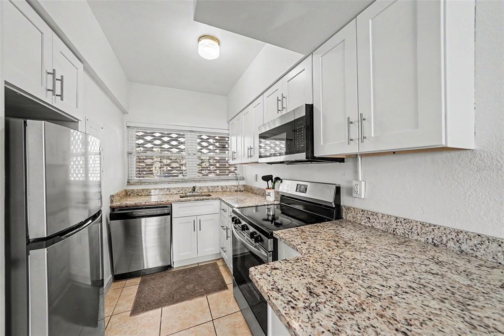 A kitchen features white cabinets, stainless steel appliances, and speckled granite countertops — 7050 SUNSET WAY UNIT 11, ST PETE BEACH, FL