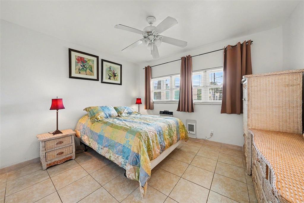 A bedroom features a bed with a colorful quilt, wicker furniture, and tile flooring — 7050 SUNSET WAY UNIT 11, ST PETE BEACH, FL