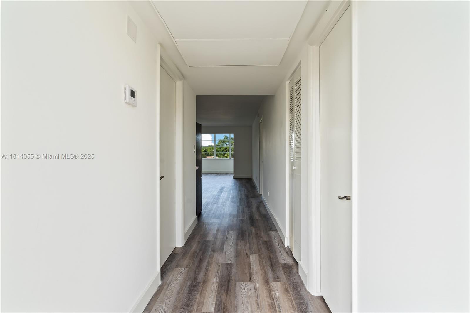 A hallway with white walls and wood-look flooring leads toward a windowed living area — 445 NE 195th St # 330, Miami FL 33179, MIAMI, FL