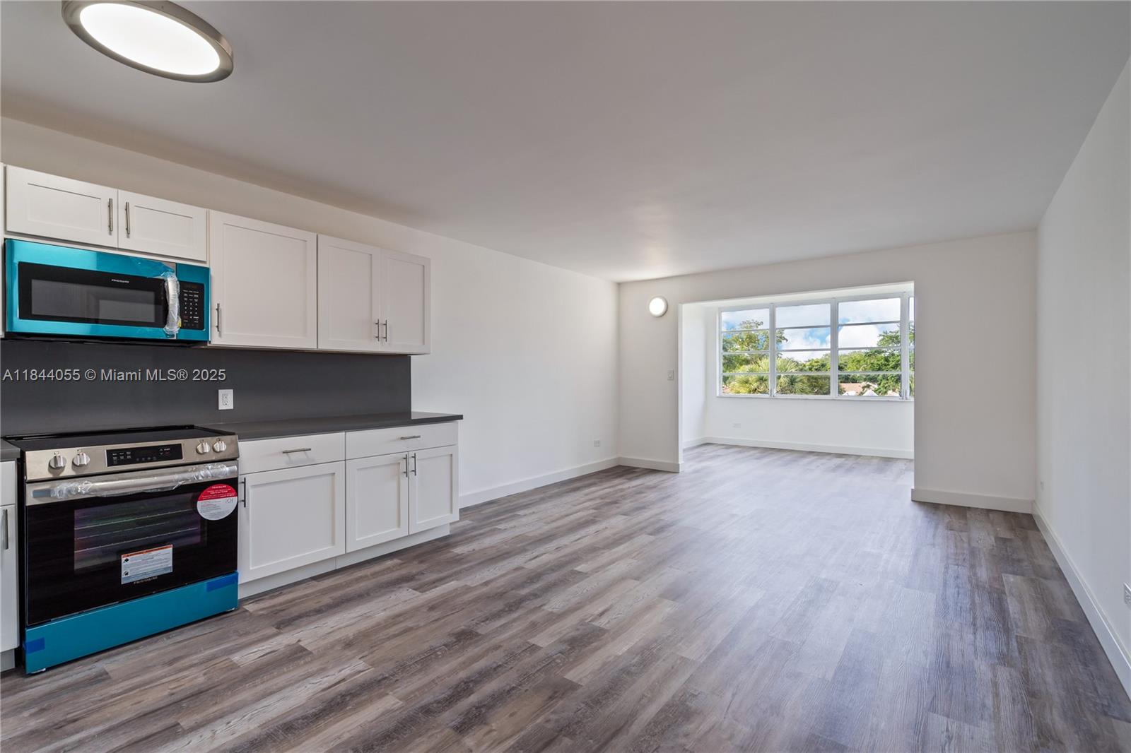A kitchen with white cabinets and a new stove opens into a bright living area — 445 NE 195th St # 330, Miami FL 33179, MIAMI, FL