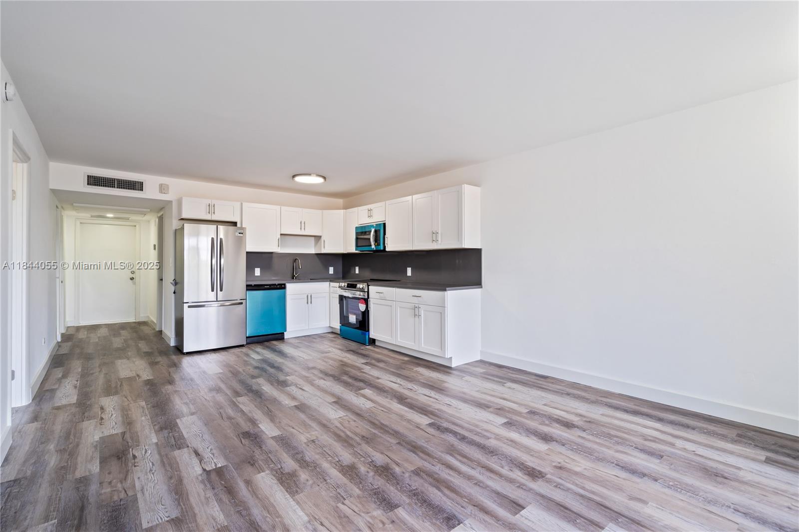 A kitchen with white cabinets, stainless steel appliances, and wood-look flooring in an open room — 445 NE 195th St # 330, Miami FL 33179, MIAMI, FL